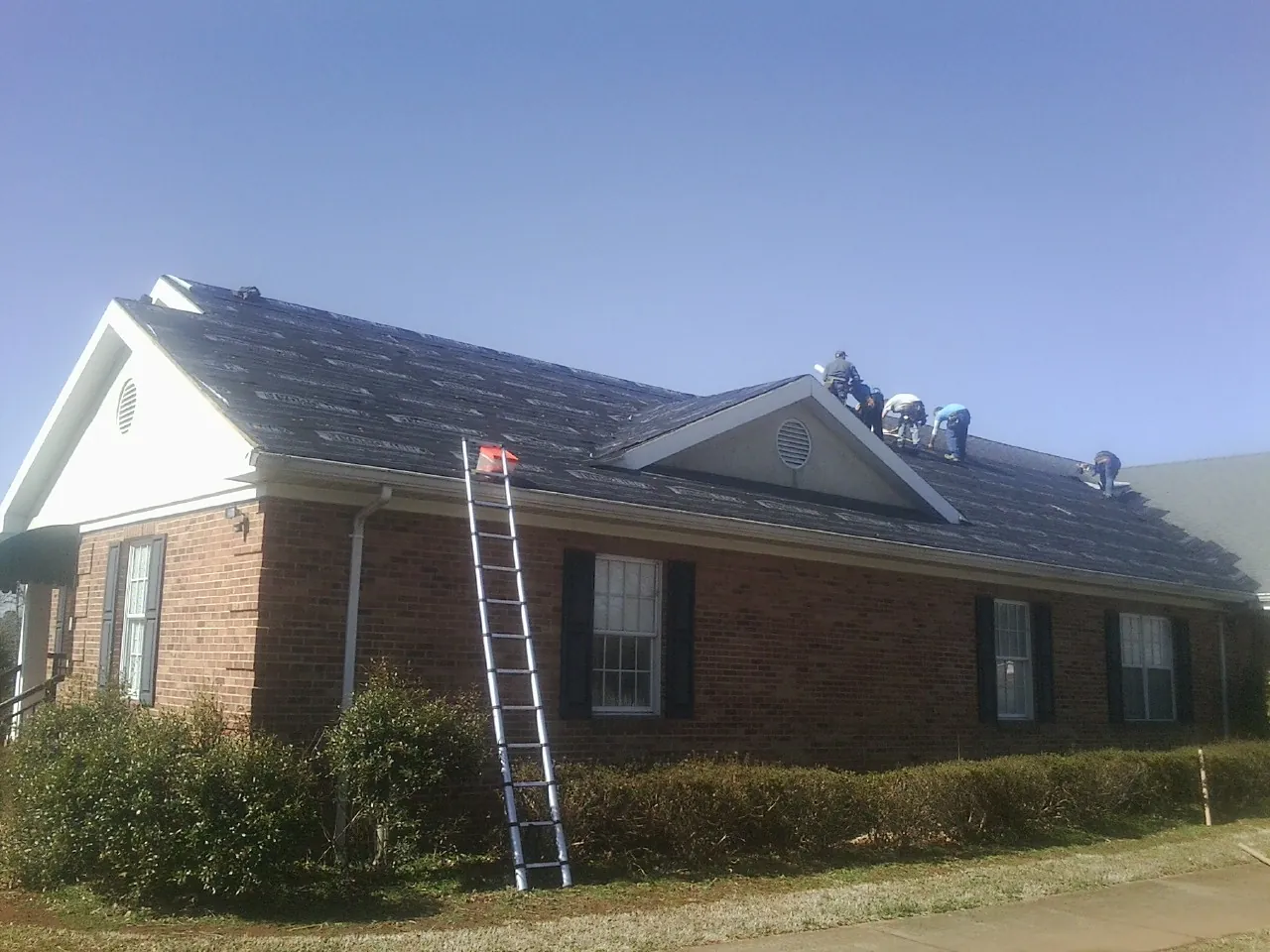 Crew tearing shingles off a brick ranch roof with a ladder set — Emergency Roof Repair work by our crew in Chantilly