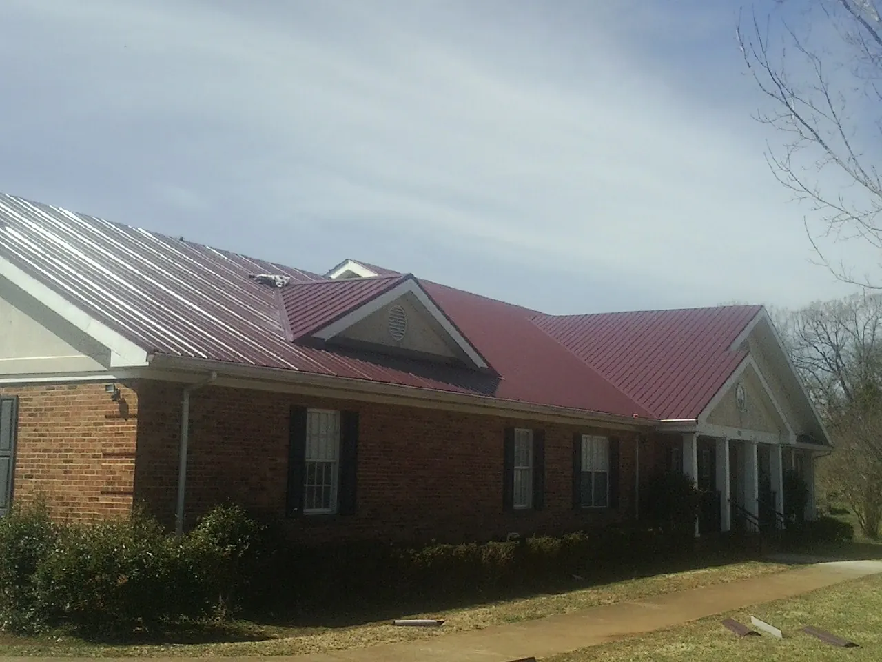 Red metal roof with gabled entries on a long brick building, from a Hail Damage Roof Repair job in Chantilly