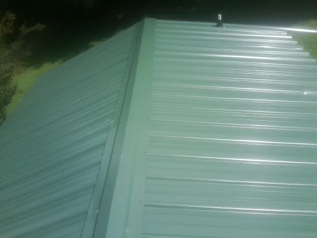 New green metal panels meeting at the ridge of a roof — Flat Roof Repair work by our crew in Chantilly