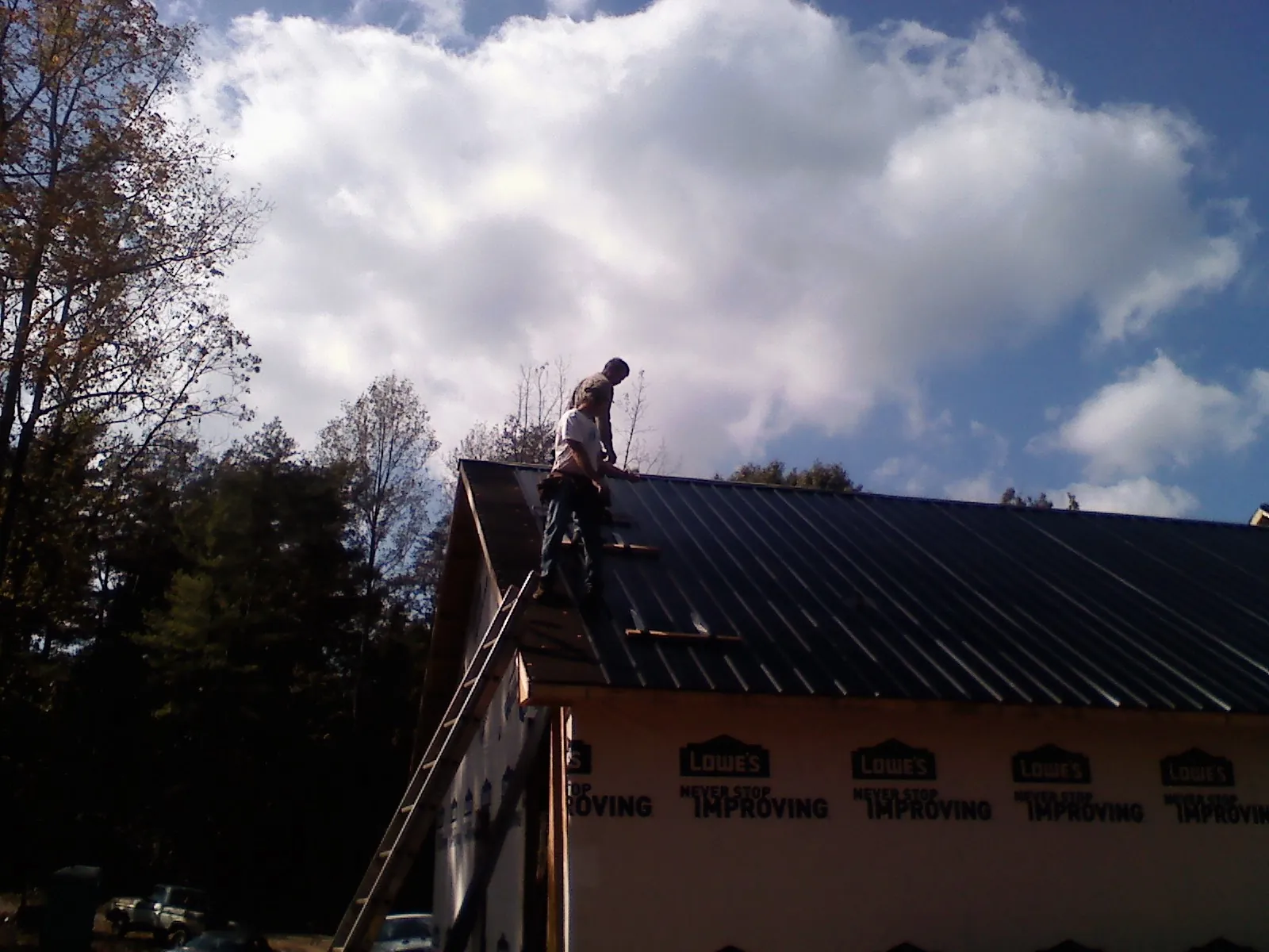 Roofer fastening dark metal panels high against a cloudy sky, from a Roof Inspection job in Chantilly