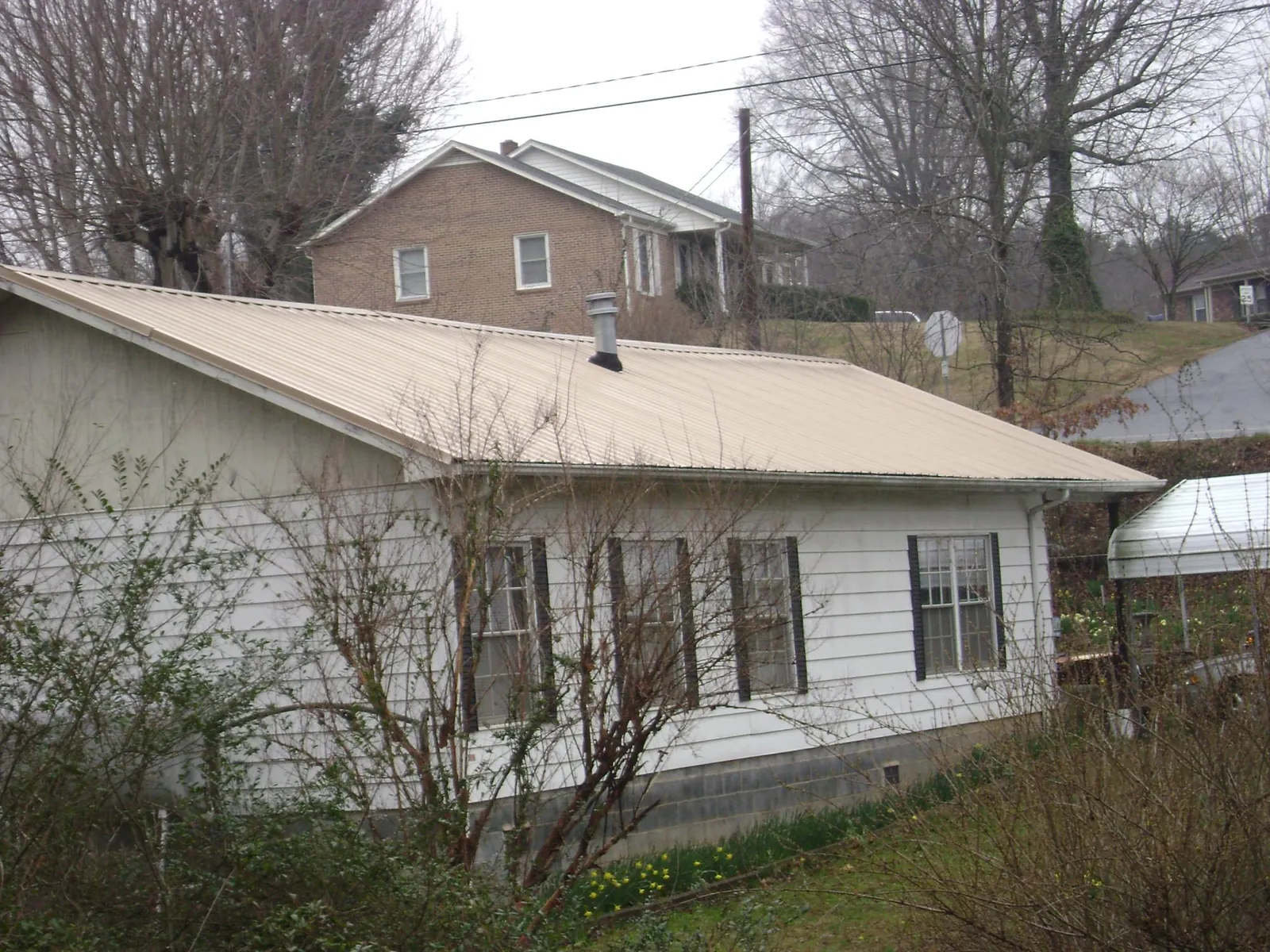 Tan metal roof on a white sided house set into a hillside — Commercial Roofing by Roofing Brothers in Chantilly